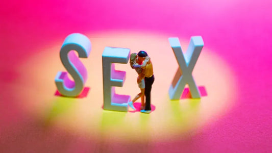 Miniature couple embracing beside 'SEX' letters on vibrant pink background