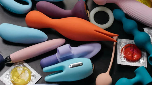 Colorful adult toys and condoms on dark surface, including vibrators and rings for intimate pleasure.