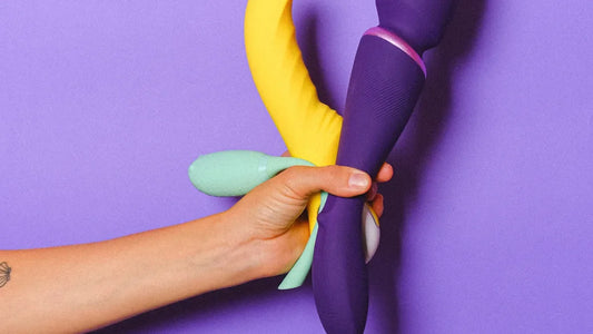 Hand holding colorful vibrators against purple background, adult toys collection