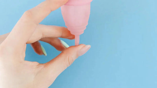 Pink silicone vibrator held in hand against blue background