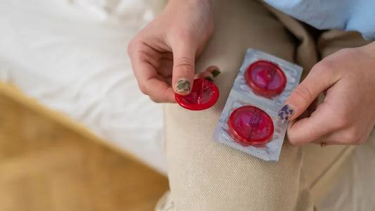 Hands holding red condoms with packaging, bedroom setting